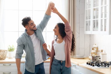 Romantik Arap eşler mutfakta dans ediyor, evde eğleniyor, modern Müslüman çift el ele tutuşuyor, gülümsüyor ve gülüyor, Orta Doğulu aşıklar birlikte vakit geçiriyorlar,