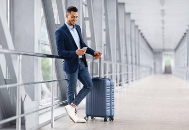 Yakışıklı Arap Havalimanında uçuşu beklerken akıllı telefonla dinleniyor, Terminalde gülümseyen Orta Doğulu erkek gezgin cep telefonu kullanıyor, Hotel Online 'da rezervasyon yaptırıyor veya İnternet' te geziniyor.