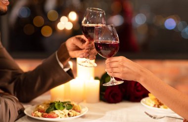 Romantik Yemek Konsepti. Restoranda oturan siyah çiftlerin elleri kırmızı şarap kadehlerini tokuşturuyor. Yaklaş, Kırpılmış