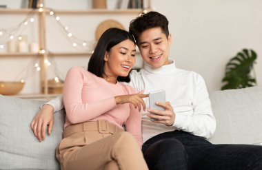 Çinli bir çift hafta sonu akıllı telefon kullanıyor. Evde koltukta oturup, akşamları birlikte geçiriyorlar. Mobil Uygulama, Telefon Kullanıcıları İnternet Taraması, Gadget Yaşam Tarzı Konsepti