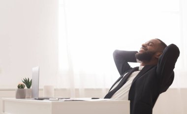 Joyful young black manager relaxing on chair in white modern office, leaning back with closed eyes, copy space
