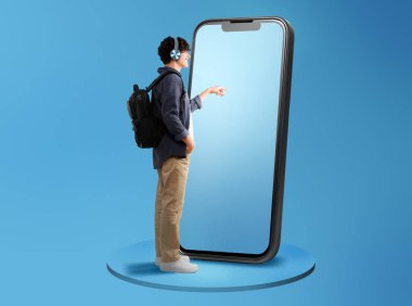 Mavi Stüdyo Arkaplanı üzerinde sırt çantalı, kulaklık takan, geniş cep telefonu dokunmatik ekranlı bir adam görüntüsü. Metin için Boş Alan, Tam Uzunlukta Panorama