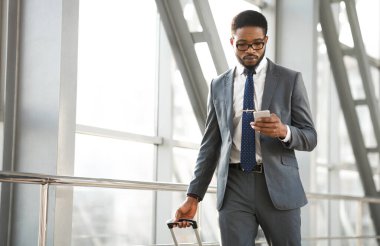 Ciddi bir iş adamı, havaalanı terminalinde seyahat çantasıyla akıllı telefondan iş seyahatinde mesaj atıyor. Boşluğu Kopyala