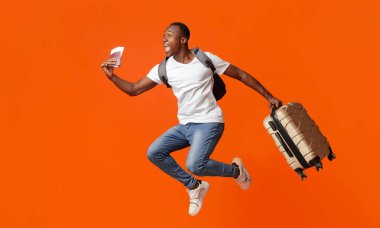 Sonunda tatil. Çantalı, sırt çantalı, pasaportlu ve turuncu atölyeli genç mutlu bir zenci. Heyecanlı Afrikalı Amerikalı adam fotokopi alanına doğru koşuyor.