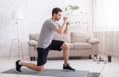 Evde spor aktiviteleri. Genç adam çevrimiçi tatbikatları izliyor ve parlak oturma odasında hareketler yapıyor.