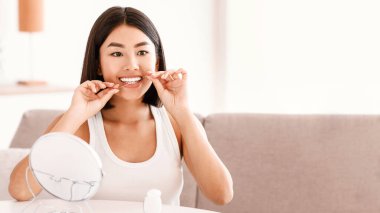 Diş sigortası ve Oral Tedavi Konsepti. Evde diş ipi kullanan kendine güvenen Asyalı kadın vlogger, yaşam tarzı blog kanalı için video kaydı, sabah rutinini gösteren, kameraya bakan
