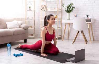 İspanyol kız evde dizüstü bilgisayarında esneme kurslarını izlerken egzersiz yapıyor.