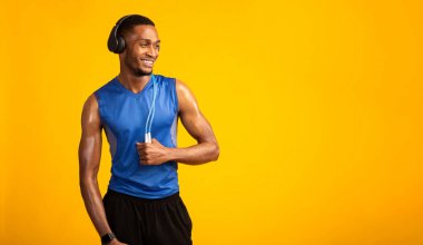 Zıplayan ipli Afrikalı kaslı adam sarı arka planda kulaklıkla müzik dinliyor. Panorama, kopyalama alanı