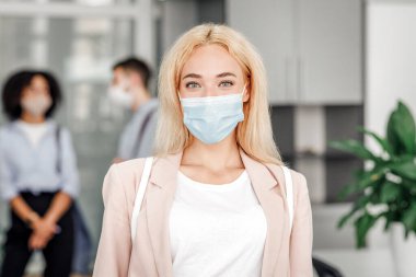 Modern yönetici karantinadan sonra işe döner ve virüse karşı korur. Koruyucu maske ve takım elbiseli çekici sarışın kadına odaklan. Ofis geçmişi bulanık çalışanlara odaklan.