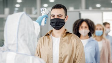 İşten önce sabah sıcaklığı kontrol ediyorum. Koruyucu maske takan işçilerde tehlikeli madde giysisi giyen adam hastalığın ilk belirtilerini kontrol ediyor.