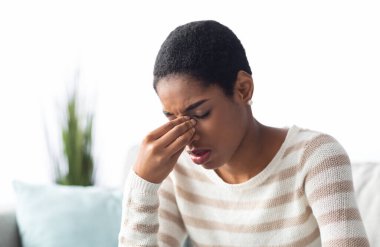 Sinüzit Konsepti. Hasta genç siyahi kadın evdeki koltukta otururken burun köprüsüne dokunuyor, Afrikalı Amerikalı kadın kendini iyi hissetmiyor, Rhinitis veya sezonluk alerjiden muzdarip,