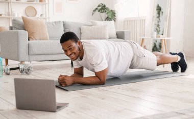 Evde eğitim. Çevrimiçi Antrenman sırasında laptopta Plank Egzersizi Yapan Siyah Adam
