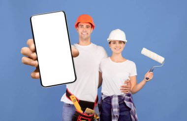 Ev tadilatı. Mavi arka planda boyama aletleri olan gülümseyen genç bir çiftin portresi. Apartman onarımına hazır, elinde boya ve tekerlekli fırçayla kovayı tutan neşeli bir adam ve kadın.