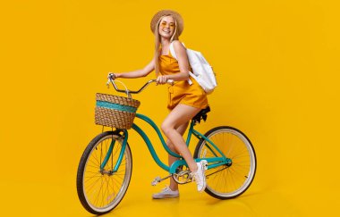Yaz Modu. Klasik bisiklete binen ve Sarı Stüdyo Arkaplanında Gülümseyen Şık Genç Kızın Uzun Boylu Portresi