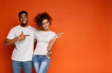 Neşeli Afrikalı-Amerikalı çift gülümseyen ve neşeyle uzağa işaret vasıl boş alan, turuncu geçmiş