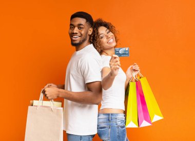 Bankamız alışveriş torbaları ve kredi kartı, turuncu arka plan ile mutlu bin yıllık bir Afrikalı-Amerikalı çift seviyoruz