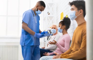 Coronavirus Covid-19 aşısı sırasında hastanede çok ırklı hastalarla konuşan Afrikalı erkek hemşire. Corona Virüsü için aşı, Kapsamlı Bağışıklık Kampanyası