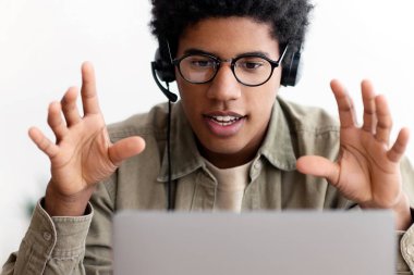 Çevrimiçi eğitim kavramı. Kulaklıklı Afro-Amerikalı genç öğrenci webinar izliyor, web konferansına katılıyor ya da dizüstü bilgisayardaki uzak mesafe dersine katılıyor. Zenci genç evden uzakta okuyor.