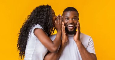 Afro-Amerikan Woman Whispering Gossips Into Her Man Ear, sarı stüdyo arka plan, panorama