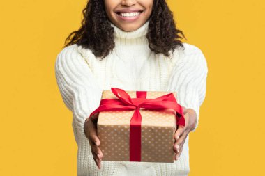 Bu hediye senin için. Afrika kökenli Amerikalı bir kadın kutusunu tutuyor ve kameraya veriyor, turuncu stüdyo arka planında izole edilmiş. Kış Tatili Kutlaması, Yeni Yıl Teklif ve Xmas Hediyeleri