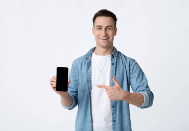 Yakışıklı adam beyaz arkaplandaki boş ekran telefonunu işaret ediyor.
