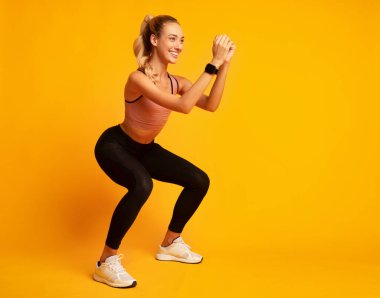 Antrenman konsepti. Stüdyoda sarı arka plan üzerine derin çömelme egzersizi yapan bir kız. Boş Alan