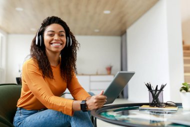 İnsanlar ve Teknoloji. Oturma odasında dijital tablet kullanan, kameraya poz veren, kablosuz kulaklıklı, gülümseyen siyah kadın portresi, bedava fotokopi alanı, afiş.