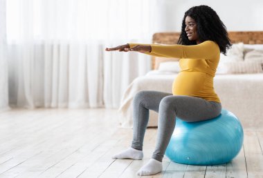Siyahi kadın baloda antrenman bekliyor, doğum için hazırlanıyor. Koca göbekli, gülümseyen Afrikalı hamile kadın yatak odasında spor salonunda oturup fotokopi odasına bakıyor. Hamilelik sırasında spor