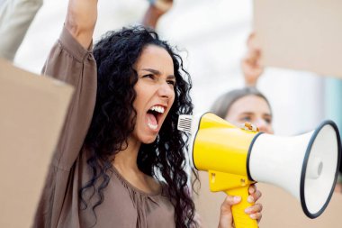 Sokakta halka açık bir toplantıda megafonla aktif melez bir kadın. Uluslararası bir grup gencin elinde boş pankartlar, ayrımcılığa veya ırkçılığa karşı protestolar var.
