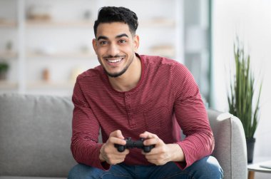 Duygusal ortadoğulu adam evde joystick ile video oyunu oynuyor, fotokopi çekiyor. Mutlu bin yıllar Arap erkeği, hafta sonunun tadını çıkarıyor, oturma odasında kanepede oturuyor, elinde joystick, kumar oynuyor.