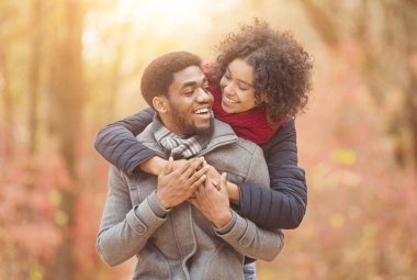 Sonbahar parkında yürüyen mutlu afro çift. Kadın arkadan sarılan adam