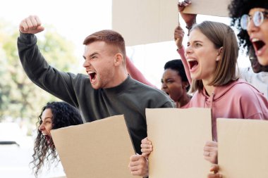 Sokakta boş afişleri olan uluslararası, motive olmuş genç göstericiler grubuna yakın çekim. Boş slogan tahtaları olan grevciler bağırıyor, yumruklarını kaldırıyor, insan hakları için mücadele ediyor, yer kopyalıyorlar.