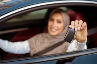 Test sürüşü yeni araba. Tesettürlü, tesettürlü, otomobil anahtarlarını camdan dışarı gösteren, araçta oturan gülümseyen Arap kadın. Kendinden emin Orta Doğulu Kadın Sürücü Koltuğu, Bulanık Arkaplan, Seçici Odaklanma