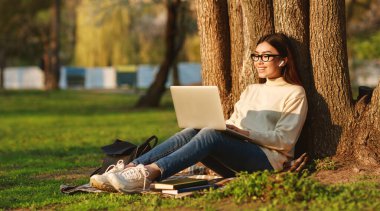 Sınavlara hazırlanın. Üniversite Kampüsünde Ağacın Altında Oturan Laptop Kullanan Asyalı Kız, boş alan panoraması