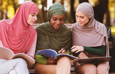 Hijab 'da, kampüs parkında oturmuş kitap okuyan üç kadın Arap öğrenci. Modern Müslüman Kadınlar İçin Eğitim