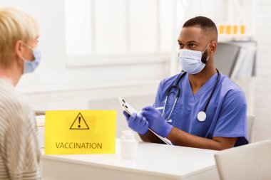 Coronavirus, Covid-19 Aşı. Hasta kadınla konuşurken not alan Afrikalı doktor Corona Virüs Aşısı olmadan önce hastanede oturuyordu. Seçici Odaklanma