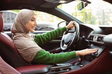 Test sürüşü konsepti. Türbanlı İslamcı Kadın 'ın profil portresi ve radyo müziği, otomobil seçeneklerini kontrol, lüks aracındaki düğmeye basma