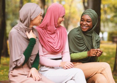 Üç farklı etnik gruptan İslamcı kadın sonbahar günü parkta bankta oturmuş tesettür takıyorlar. Mutlu Müslüman Kadın Dostları Sohbetin Tadını Çıkartıyor. Arkadaşlık Konsepti