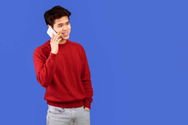 Her zaman temastayız. Sıradan gülümseyen Asyalı adamın portresi akıllı telefonuyla konuşuyor, yan tarafa bakıyor, mavi stüdyo arkaplanı, afişi, fotokopi alanı üzerinde soyutlanmış ve poz veriyor. İletişim, Telefon Çağrısı