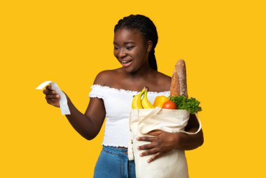 Alışveriş Ekonomisi. Paket dolusu yiyecek ve makbuz taşıyan, çantalarını taşıyan, sarı stüdyonun arka planında duran, fotokopi çeken, çantalarını dolduran,