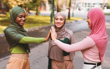 Üç farklı İslamcı kadın dışarıda park yerinde başörtüsü takarak beşlik çakıyor. Müslüman Kadınlar Konsepti, Arkadaşlık, Birliktelik ve Birlik