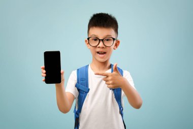 Eğitim Uygulaması. Elinde boş bir siyah ekranla akıllı telefonu işaret eden heyecanlı Asyalı liseli çocuk mavi arka planda yeni bir uygulama öneren sırt çantası takan erkek çocuk,