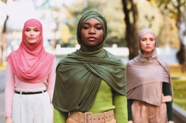 Dışarıdaki parkta kameraya bakan üç farklı müslüman kadın pozu. Çok Kültürlü İslami Bayanların Grup Portresi, Türbanlı Afrikalı Amerikalı Kadın Üzerine Seçici Odaklanma