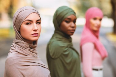Üç Ciddi Müslüman Kadın, dışarıda sıraya girmiş kameraya bakıyormuş gibi görünüyor. Çok ırklı Müslüman Kadınların Grup Portresi. Arapça Kadın Çeşitliliği Konsepti