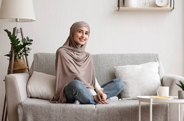 Evdeki kanepede poz veren tesettürlü gülümseyen Arap kız portresi oturma odasında rahat bir kanepede dinleniyor, hafta sonunun keyfini çıkarıyor.