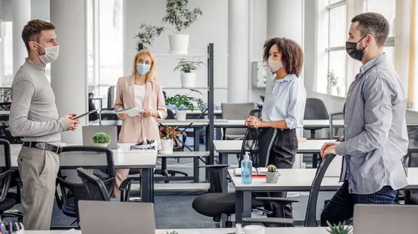 İş arkadaşlarıyla yaratıcı fikirler ve iş planları hakkında acil bir toplantı. Koruyucu maskeli çok ırklı meslektaşlar sosyal mesafeyi koruyorlar ve ofisteki CV19 'da yeni normalleri tartışıyorlar.
