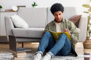 Web tabanlı eğitim. Odaklanmış siyah bir genç evdeki dizüstü bilgisayara çevrimiçi derste bilgi yazıyor. Zeki Afrikalı Amerikalı adam internet konferansı sırasında not alıyor ya da özel öğretmenle görüşüyor.