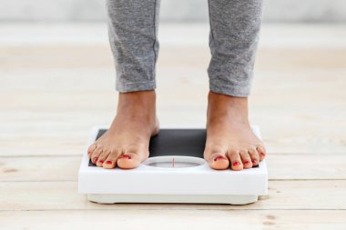 Kapalı alanda terazide dikilen, ağırlığını ölçen, ayak manzarası kesilen genç Afrikalı Amerikalı kadın. Zayıflama diyetindeki tanınamaz siyah kadın. Sağlık hizmetleri kavramı