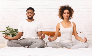 Zihinsel birlik. Sakin Afrikalı çift birlikte meditasyon, yatakta lotus pozisyonda oturan, panorama