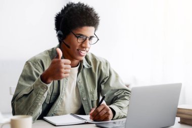 Mesafe iletişimi. Neşeli Afrikalı Amerikalı adam dizüstü bilgisayara el hareketi yapıyor, internette arkadaşı ya da öğretmeniyle konuşuyor. İnternet konferansına katılan siyah öğrenci